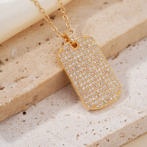 Golden rectangular pendant necklace with paved clear zircons on beige stone background