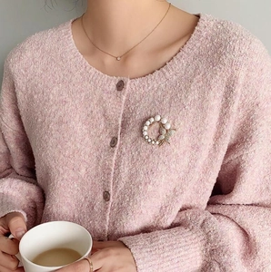 Detailansicht einer eleganten Perlenbrosche mit Strass-Schmetterling auf rosa Strickjacke
