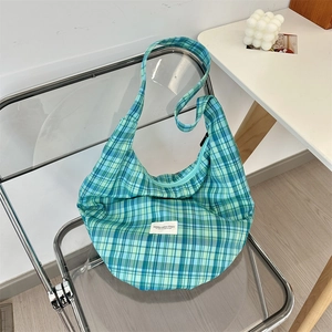 Detail of blue and green plaid canvas hobo bag texture with a minimalist white logo patch