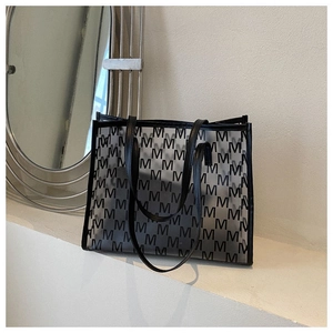 Detail of transparent PVC tote bag with M-letter print and black leather handles