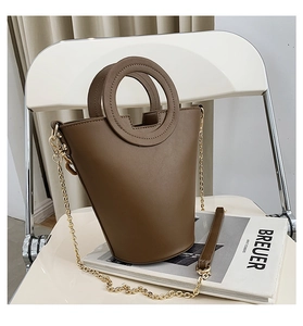 Detail of minimalist brown bucket bag with circular handles and gold metal chain strap