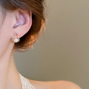 Close-up of golden teardrop pearl earrings worn by a model in soft elegant lighting