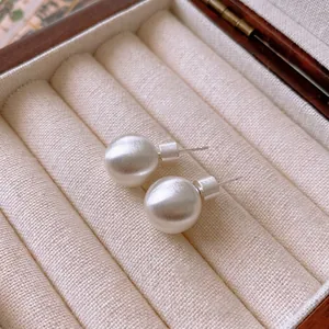 Minimalist matte silver round stud earrings displayed in a luxury wooden jewelry box