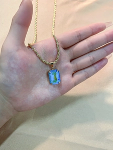 Detail of square blue-green zircon pendant on a golden twist rope chain held in hand