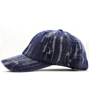 Detailed side view of dark blue distressed denim baseball cap with frayed hole accents