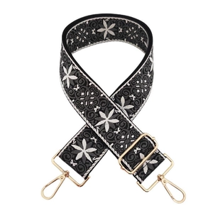 Detailed close-up of ethnic black and white floral embroidery on a wide bag strap with gold hooks