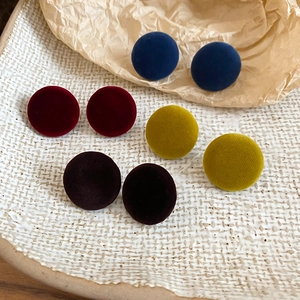 Detailed view of round velvet earrings in navy, burgundy, yellow, and brown on a ceramic tray