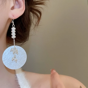 Detailed close-up of a long pearl drop earring with large textured white circular pendant
