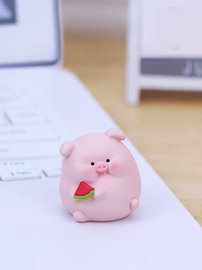 Close-up of cute pink resin pig figurine holding a watermelon on an office desk