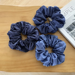 Three pieces of dark blue denim elastic hair scrunchies on a minimalist wooden table