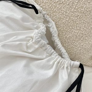 Detail of white linen drawstring bag with black woven cord on soft textured background