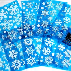 Flat lay view of various white snowflake static cling stickers on blue backing paper