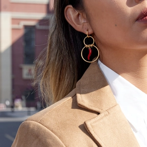 Close-up of gold double hoop earrings with a red chili pendant on a model