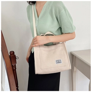 Model wearing a beige corduroy tote bag with long strap and small woven label detail