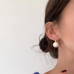 Close-up of model wearing white pearl earrings with golden metal clasps