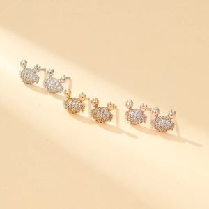 Macro detail of crab-shaped studs in silver, gold, and rose gold with zircon inlay