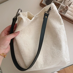 Detail of floral lace embroidery on beige cotton tote bag with a black leather strap