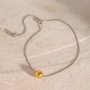 Adjustable silver snake chain bracelet with a polished gold bead detail on stone surface