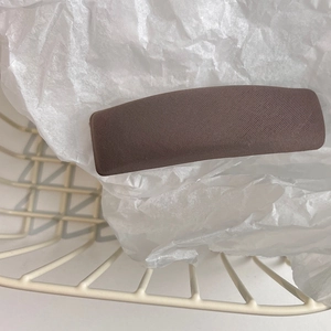 Close-up of a matte dark brown fabric sponge hair clip on a minimalist textured background