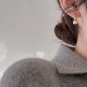 Close-up of elegant gold hoop earrings with white pearls worn on a female model