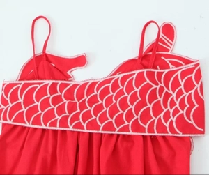 Détail d'une robe rouge à bretelles avec broderie d'écailles blanches sur la poitrine