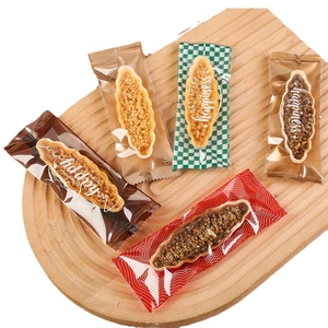 Five assorted boat-shaped nut tarts in colorful sealed plastic bags on a wooden tray