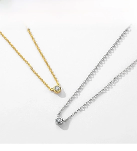 Detailed view of silver and gold necklaces with minimalist round zircon pendants