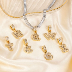 Elegant gold letter pendants and sparkling tennis necklace on a beige silk background