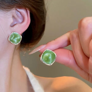 Macro view of green resin stud earrings with silver frame worn on ear for detail