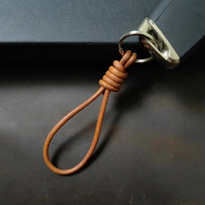 Handcrafted brown leather keychain with metal ring and remote key on a dark leather texture