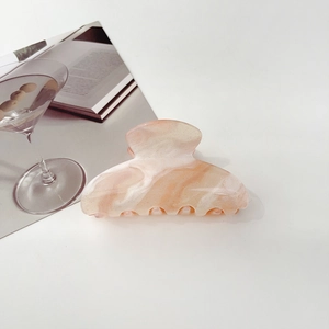 Pink marble hair claw clip with golden glitter shown on a clean desktop with magazine