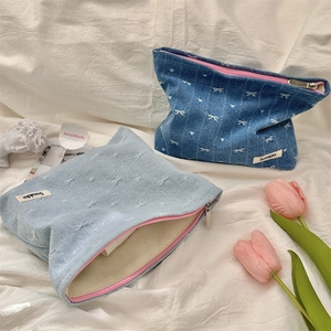 Close-up of denim cosmetic bag with white bow embroidery and pink zipper detail
