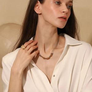 Close-up of model wearing gold-plated beaded necklace and oval white gemstone ring