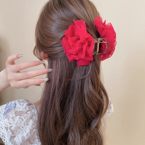 Detailansicht einer roten Chiffon-Blumen-Haarklammer in braunem welligem Haar