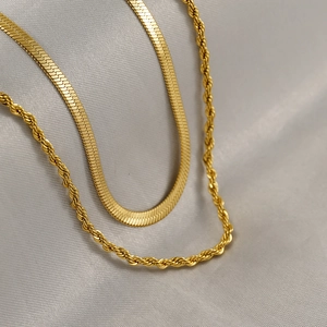 Close-up of gold snake chain and twisted rope necklace set on elegant grey silk fabric