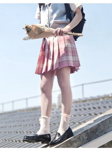 Close-up of beige crew socks with delicate bow detail worn with a pink plaid pleated skirt