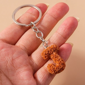 Detailed view of resin orange rose letter J keychain with silver ring held in hand