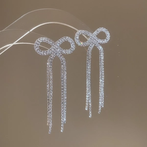 Detail of silver bow tassel earrings with sparkling crystals hanging on a clear stand