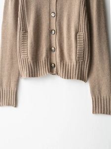 Detail of camel chunky knit cardigan featuring tortoise shell buttons and ribbed pockets