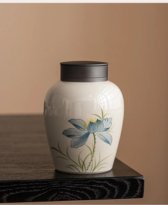 Detail of a beige ceramic tea canister with a blue lotus flower on a wood surface