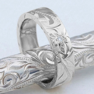 Macro view of silver Hawaiian floral engraving and solitaire diamond on the ring band