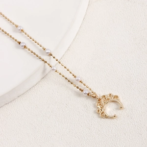 Détail d'un collier doré orné de perles blanches et d'un pendentif lune couronne
