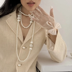 Detail of layered pearl necklace with diamond-studded balls on tweed jacket and lace gloves
