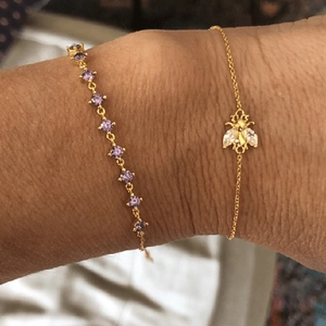 Close-up of a gold bee bracelet with purple gemstones on a model's wrist detail