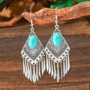 Detail of vintage teardrop earrings with turquoise stones and fringes on wooden branch