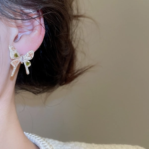 Detail of elegant gold butterfly earring with green stones and zircon on model's ear