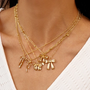 Détail de cinq colliers dorés superposés avec pendentifs nœuds portés sur un modèle