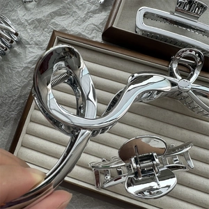 Detailed view of silver metallic shark hair clips with twisted knot designs in a beige tray