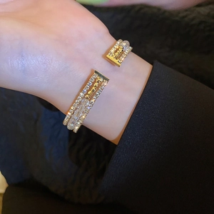 Close-up of gold open cuff bracelet with white beads and rhinestones on a wrist