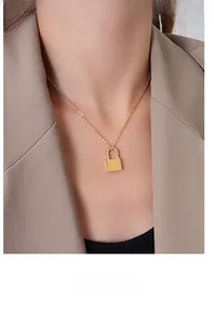 Close-up of a polished golden square padlock pendant necklace worn by a model